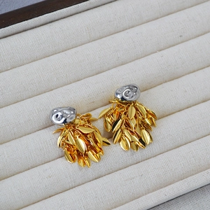 Close-up of gold leaf tassels and silver textured stud earrings on beige fabric tray