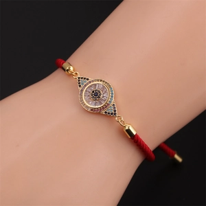Gros plan d'un bracelet œil porte-bonheur avec cordon rouge et pendentif doré en zircon