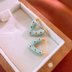 Boucles d'oreilles cœur en émail vert à pois rouges avec bordure dorée sur velours