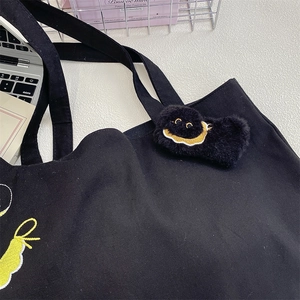 Close-up of yellow cartoon embroidery and plush pendant on black canvas tote bag
