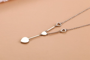 Detail view of silver Y-shaped necklace featuring dual heart pendants on a beige background