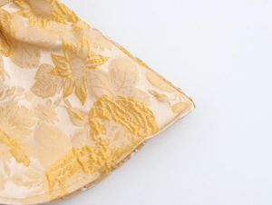 Makroansicht goldener Stickerei auf beigem ärmellosem Top zeigt die Stoffstruktur