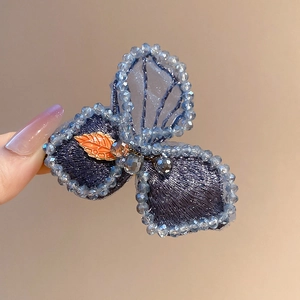 Detail of blue mesh butterfly hair clip with hand-embroidered beads and enamel leaf ornament