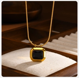 Detail shot of a square dark zircon pendant on a gold snake chain over a jewelry box