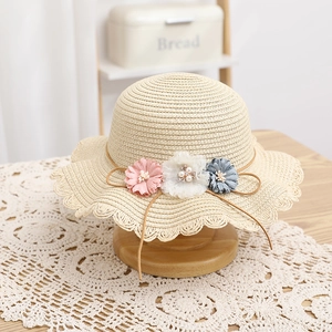 Dettaglio di un cappello di paglia per bambini con tre fiori delicati e bordo in pizzo ondulato