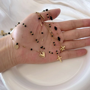 Gold layered black bead necklace with starfish heart and cross charms on white tray