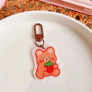 Close-up of cute acrylic bear keychain with strawberry on a white ceramic plate and tray