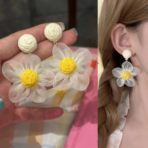 Vista macro detallada de pendientes de flores de rafia hechos a mano en la oreja y mano