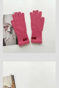 Detailed view of knitted pink and blue gloves featuring delicate red bow embroidery detail