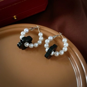 Close-up of vintage flower earrings with white pearls and black acrylic petals on ceramic tray