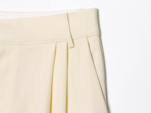 Détail du pantalon plissé crème avec tissu texturé et savoir-faire de la ceinture ajustée