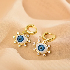 Close-up of gold evil eye hoop earrings with blue stones on pink satin fabric