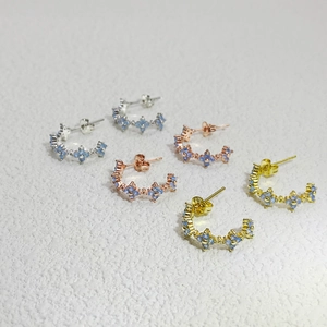 Detailed view of C-shaped floral earrings in gold, silver, and rose gold with blue zircons