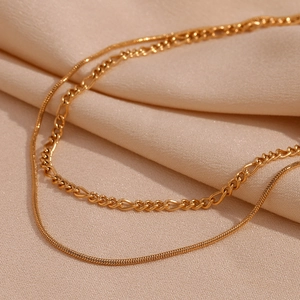 Close-up of dual-layer 18K gold plated snake and Figaro chain necklace on silk fabric
