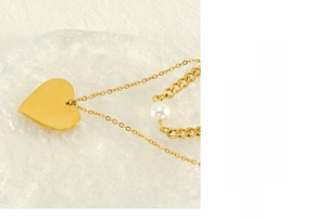 Detail of a gold double-layer necklace with heart pendant and white pearl charm