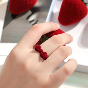 Red velvet bow ring worn on finger next to strawberry props in a minimalist setting