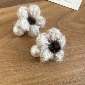 Elegant knit flower stud earrings with large white pearls on a natural wood surface