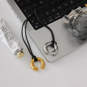 Detailed shot of gold and silver horseshoe necklaces on black cords with lifestyle props