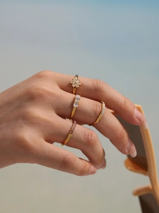 Detail of stacked gold zircon flower rings on hand holding sunglasses in natural light