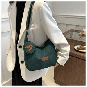 Detail of dark green corduroy shoulder bag with letter A coin purse on a white blazer