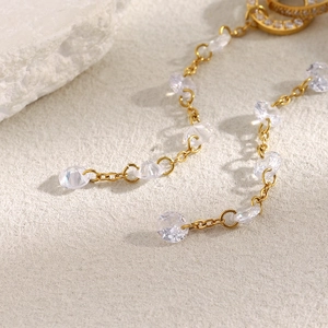 Detail of 18K gold-plated chain earrings with faceted clear crystals on textured stone