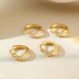 Minimalist V-shaped gold hoop earrings with white zircon on elegant satin texture