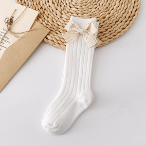 Detail view of white ribbed cotton toddler socks with a large cream bow on a wooden mat