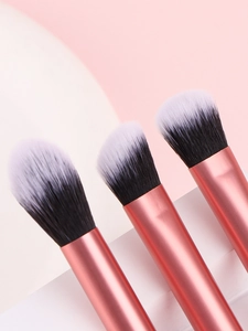 Gros plan de trois pinceaux de maquillage roses avec manches en or rose sur supports