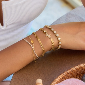 Detailed view of layered gold heart and geometric charm bracelets worn by a model