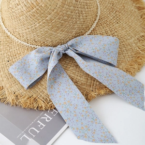 Détail d'un chapeau de soleil en raphia avec ruban fleuri et chaîne de perles