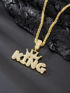 Detail view of gold iced out KING pendant with crown on twist rope chain over black rocks