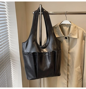 Detailed view of a black leather tote bag with two front pockets hanging on a rack