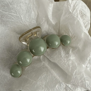 Close-up of Morandi green pearl hair claw clip on soft white wrinkled paper