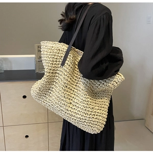 Detail of a beige woven straw tote bag featuring a premium dark brown leather shoulder strap