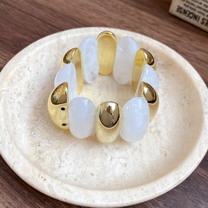 Detail of chunky gold and marble acrylic elastic bracelet on a stone tray display