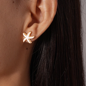 Detailed close-up of a gold starfish earring with white enamel inlay on a model