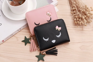Detail of pink and black PU leather cartoon wallets with bow and tassel on wooden desk