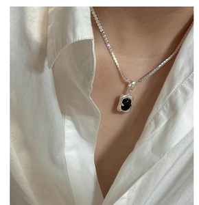 Macro detail of a silver S925 necklace with a black onyx pendant worn on a female model