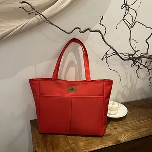 Minimalist red nylon tote bag with dual front pockets and leather label on wooden stand