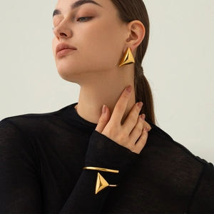 Dettaglio degli orecchini geometrici e bracciale rigido in acciaio dorato sul modello