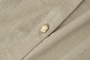 Macro detail of beige faux linen fabric and irregular gold button on sleeveless dress