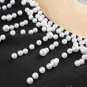 Détail des perles blanches cousues sur la robe de soirée noire à col montant