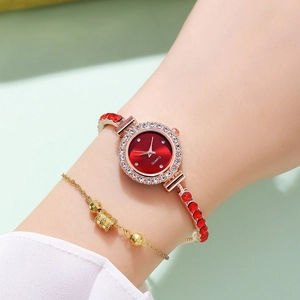 Detail view of a luxury gold women's watch with red dial and sparkling rhinestone accents