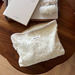 Détail de la broderie en dentelle sur trousse à cosmétiques crème avec étiquette en tissu