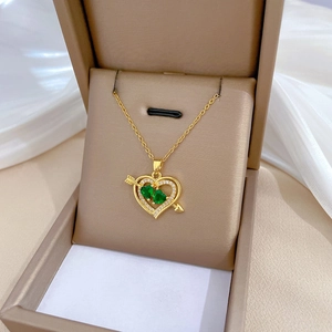 Close-up of golden heart pendant with green gems and arrow in a beige jewelry box