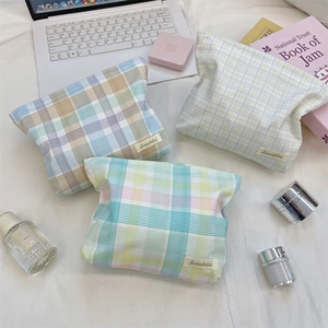 Detailed view of three plaid cosmetic bags in rainbow colors on a white bed sheet
