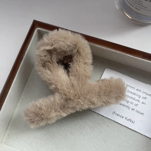 Dettaglio di una morbida pinza per capelli in peluche beige su un vassoio di legno minimal