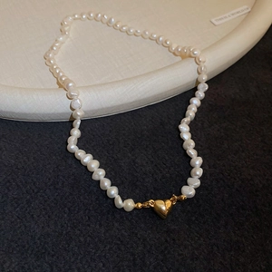 Macro shot of 18K gold heart magnetic clasp on white baroque freshwater pearl necklace