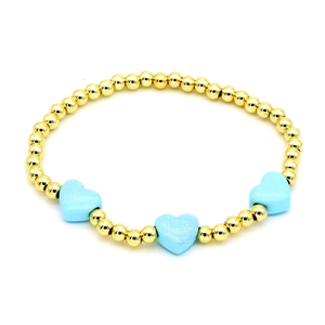 Detail of gold beaded bracelet featuring three light blue enamel heart charms on white background