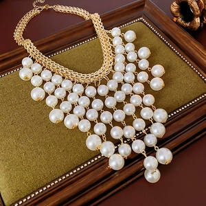 Dettaglio di collana dorata con nappe di perle bianche su espositore in velluto